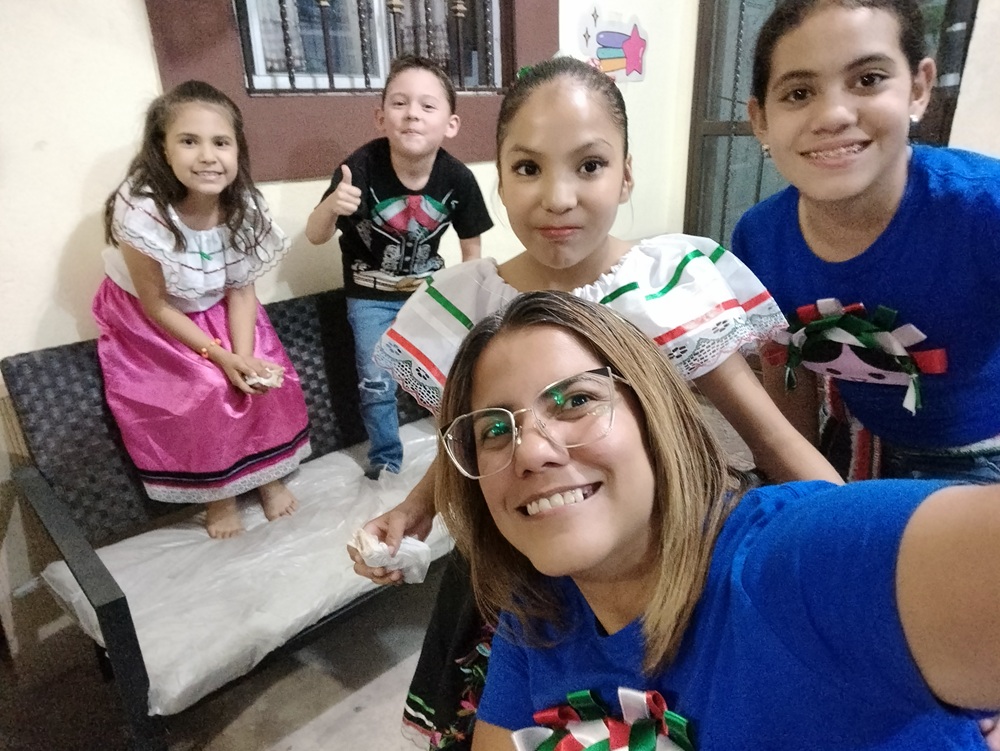 Mujer tomándose una selfie con niñas y niños, algunos con vestimenta tradicional mexicana.