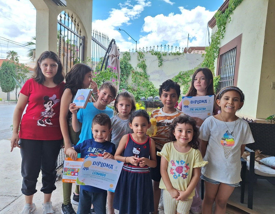 Niñas y niños mostrando diplomas al aire libre.